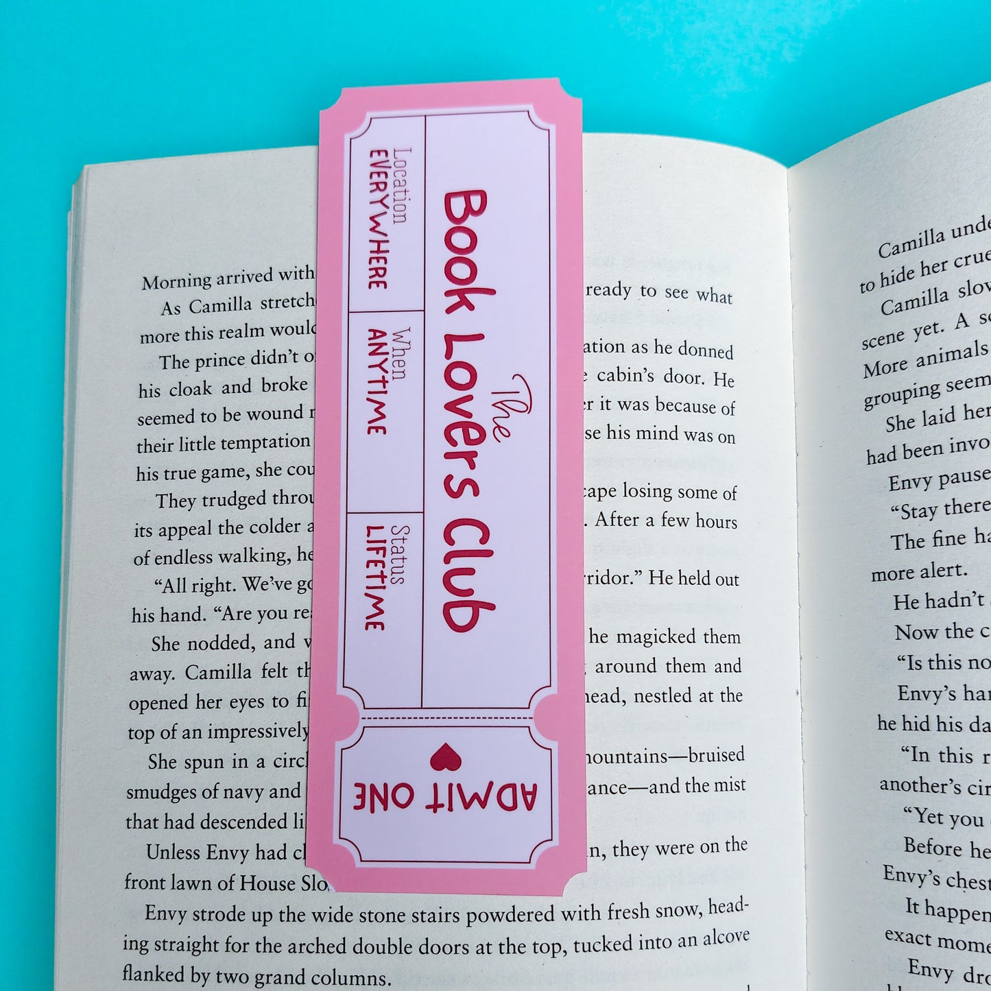A pink and white 'The Book Lover's Club' admission one ticket displayed on an open book page with printed text.