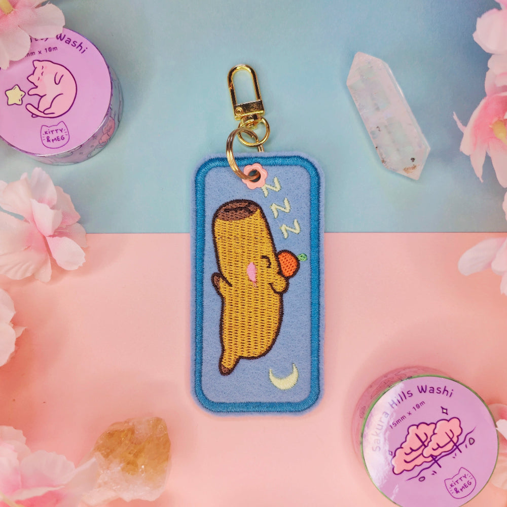 Embroidered keychain with a sleeping character on a floral and pink background