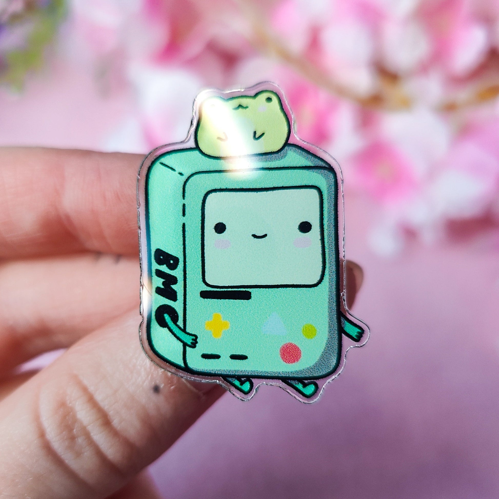 Cute BMO-inspired acrylic pin with a frog on his head, displayed on art backing card