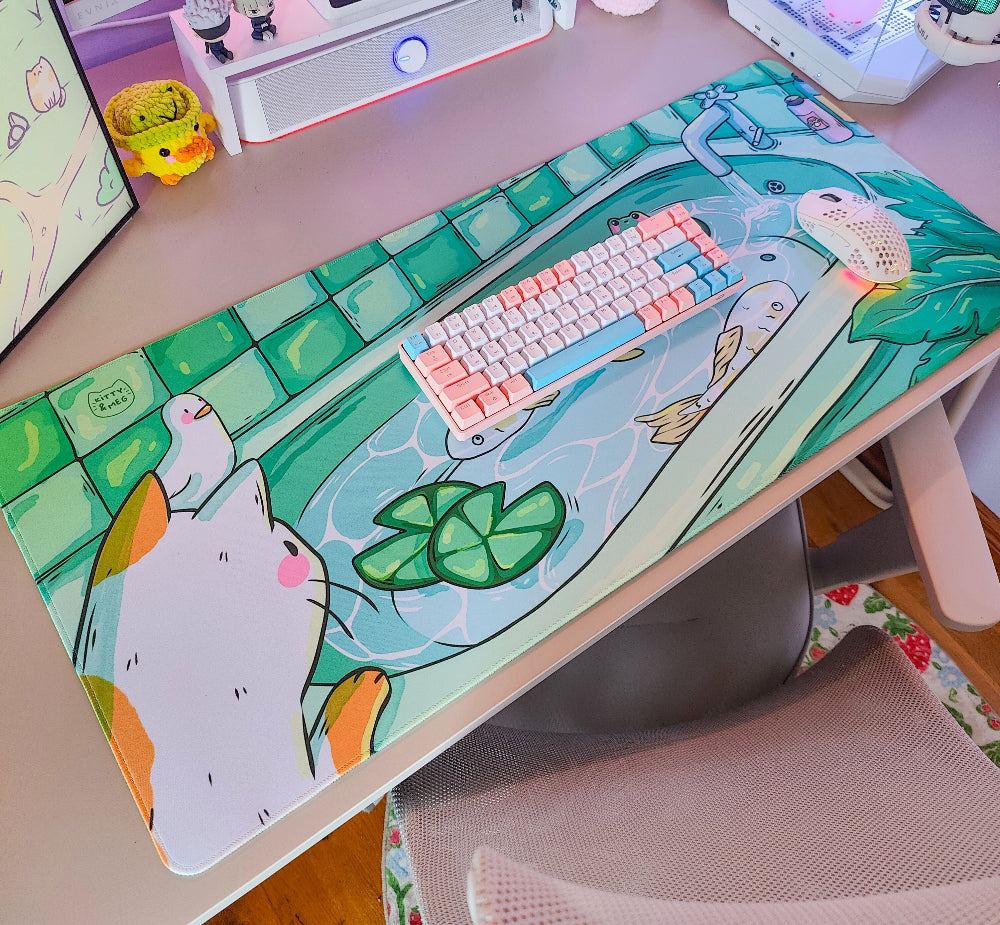 Desk setup with a colorful desk mat featuring cartoon fish and lily pads, a keyboard, and a computer monitor.