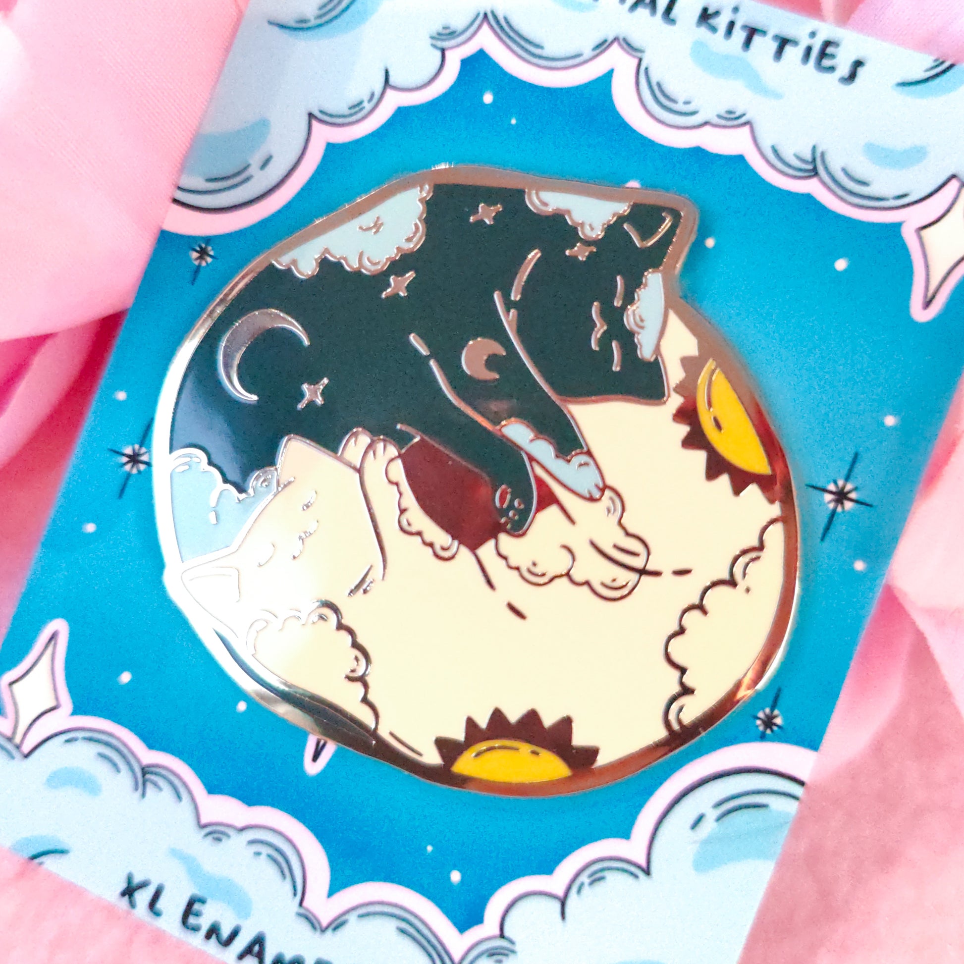Enamel pin of a cat on a moon with a blue card featuring stars and clouds.