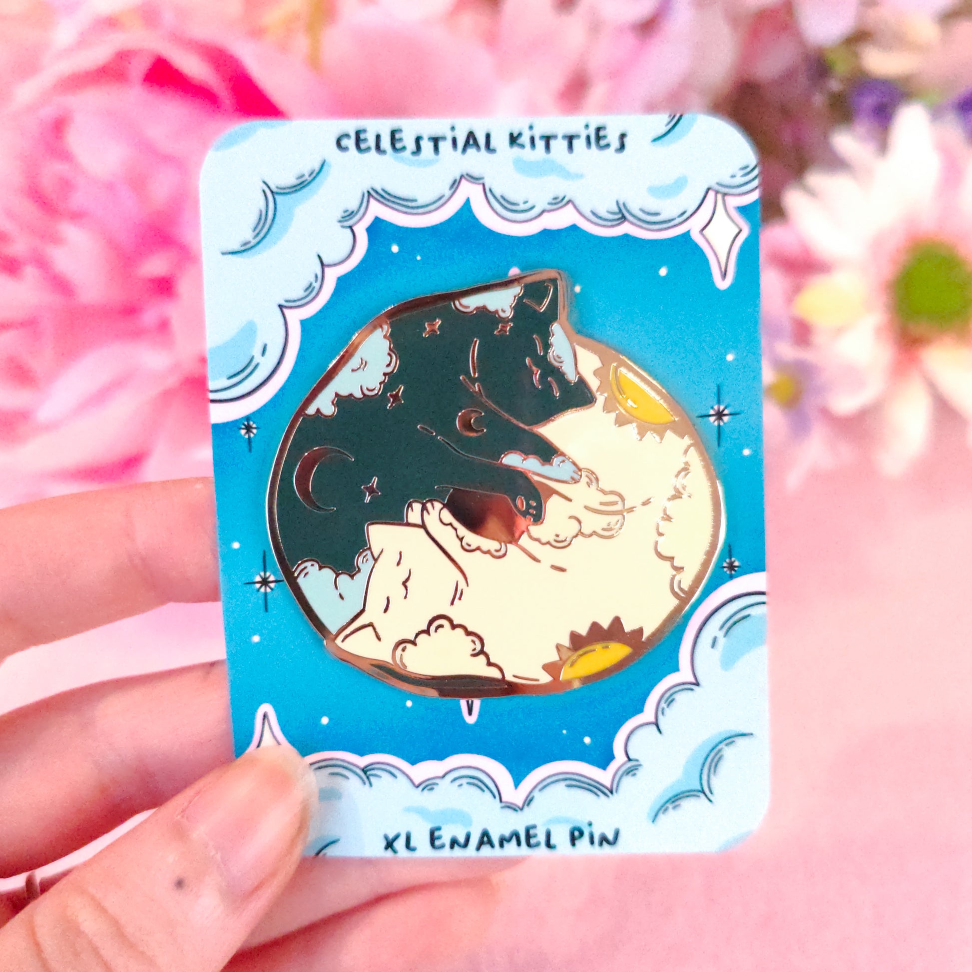 Enamel pin with celestial design on a blue card, surrounded by pink flowers. shipped from eu
