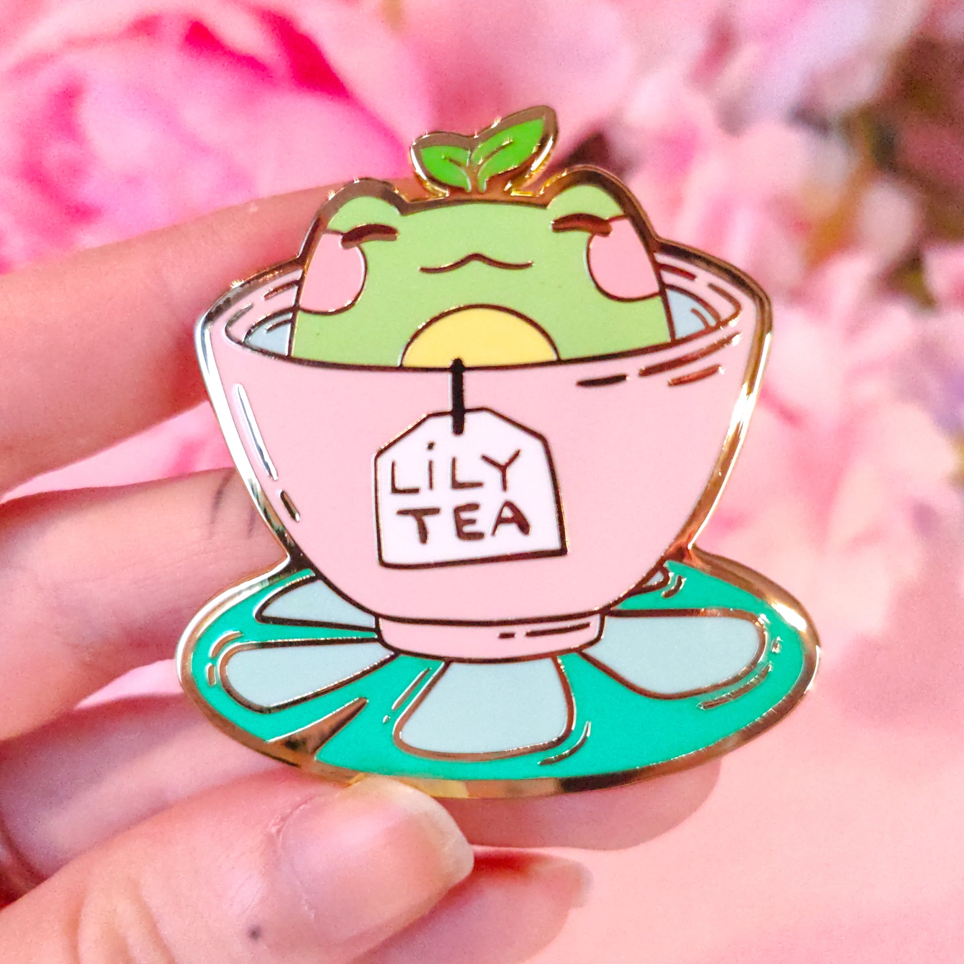 Enamel pin of a frog in a teacup with 'Lily Tea' label against a pink floral background