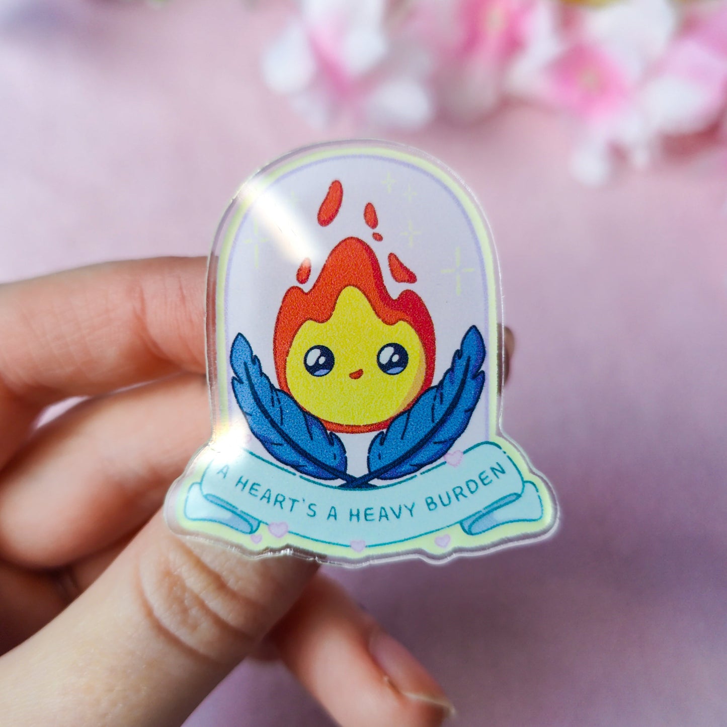 Calcifer-inspired flame spirit acrylic pin with quote ‘A heart’s a heavy burden’ on backing card