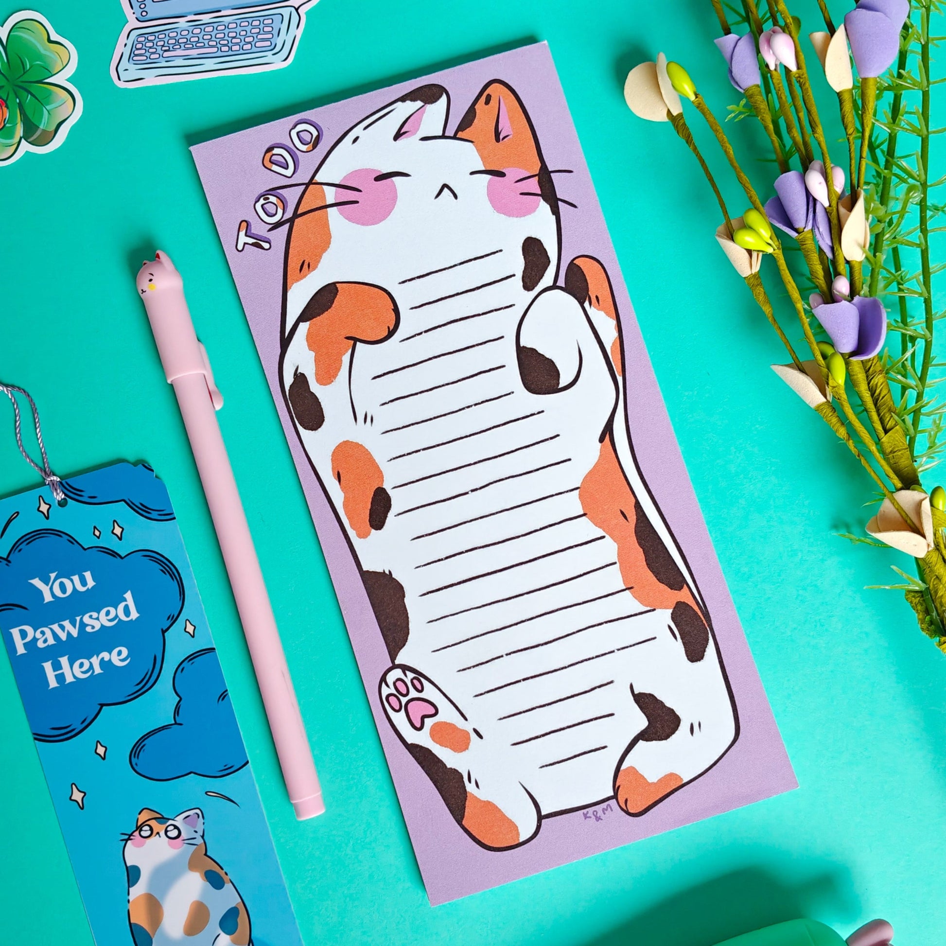Cat-themed notepad with a pen and decorative items on a teal background