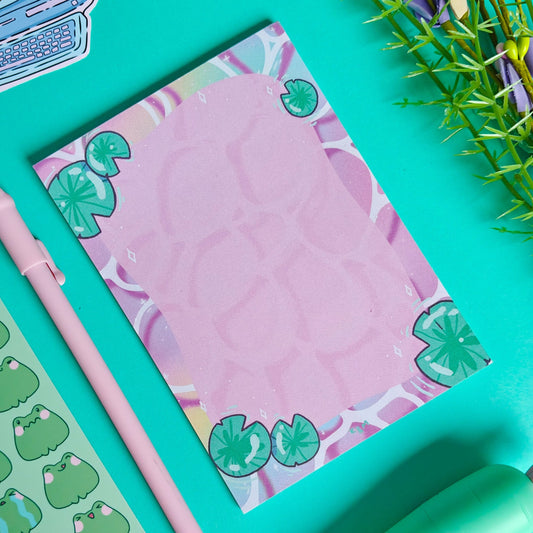 Notebook with green leaf design, pink pen, and green stickers on a teal background