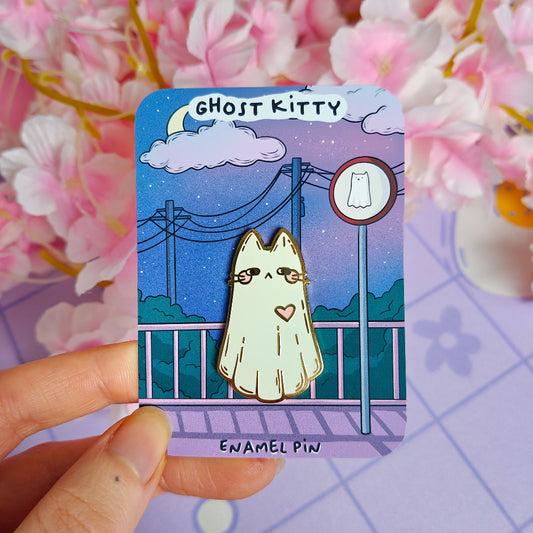 Ghost Kitty enamel pin on a card with a hand holding it, against a floral background.