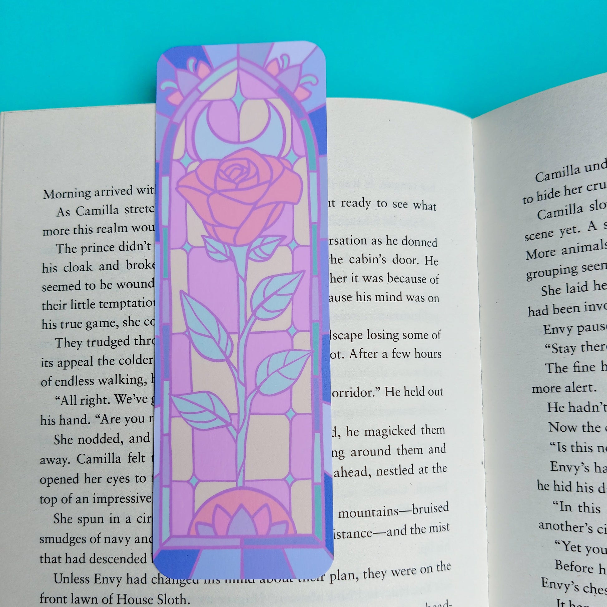 A colorful paper bookmark with a pink rose design and the word 'LOVE' printed in purple, placed on open book pages against a bright blue background.
